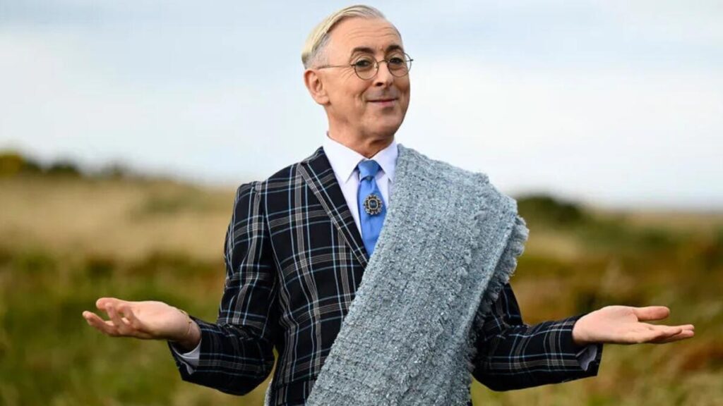 Alan Cumming smiling at an event, representing his career success, entrepreneurial ventures, and financial achievements.