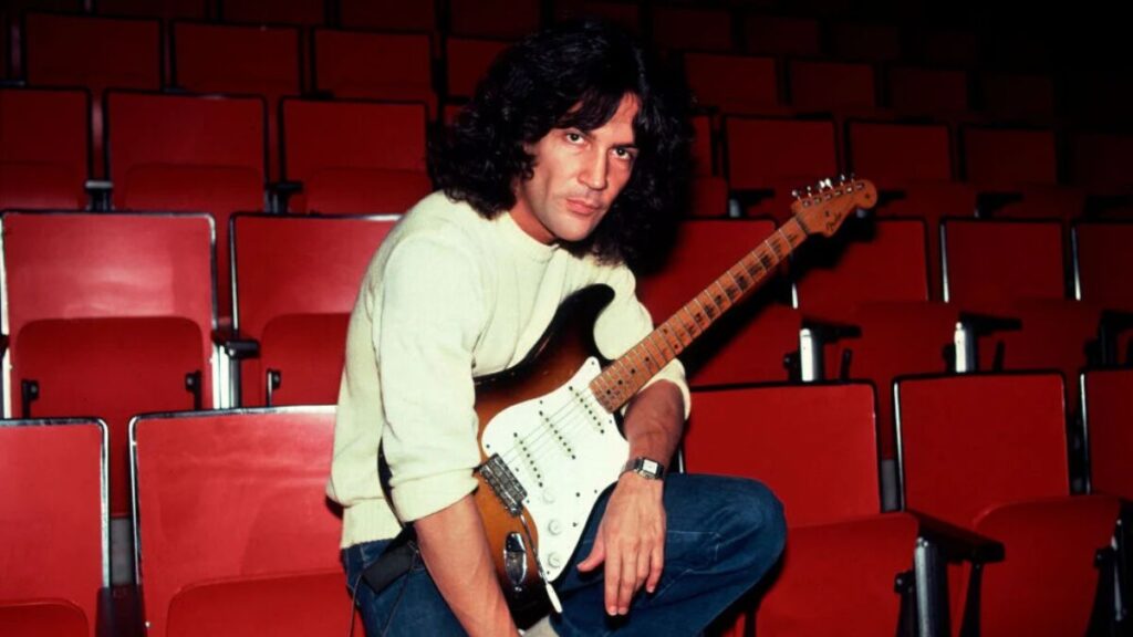 Billy Squier holding a guitar, highlighting his legacy as a classic rock icon.