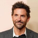 Bradley Cooper smiling at a event, wearing a classic suit.