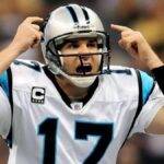 Jake Delhomme passionately shouting instructions during an NFL game with the Carolina Panthers, wearing team uniform and helmet.