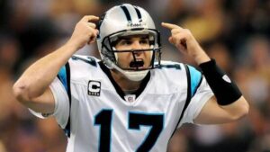 Jake Delhomme passionately shouting instructions during an NFL game with the Carolina Panthers, wearing team uniform and helmet.