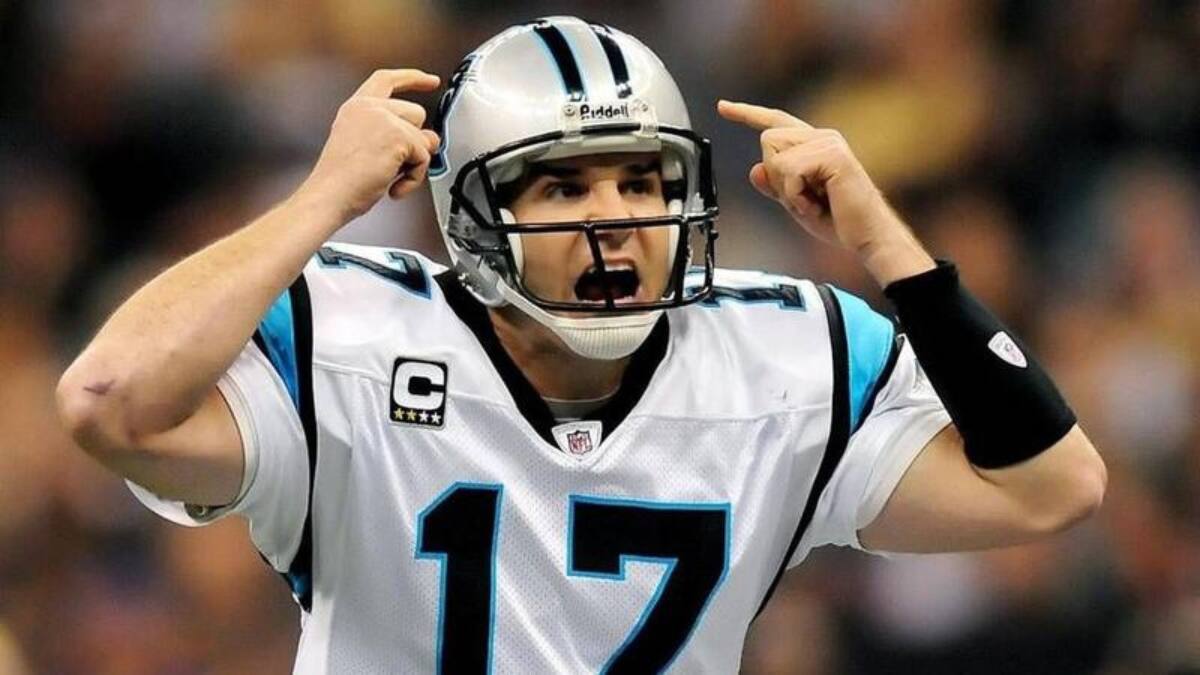 Jake Delhomme passionately shouting instructions during an NFL game with the Carolina Panthers, wearing team uniform and helmet.