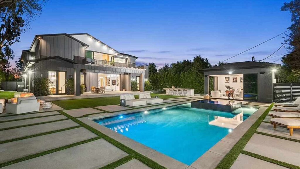 Exterior view of Madison Beer’s modern farmhouse-style home in Los Angeles, featuring white paneling, large windows, and landscaped front yard.