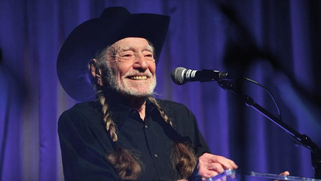 Willie Nelson performing live on stage with guitar, wearing trademark bandana — highlighting his decades-long country music career.