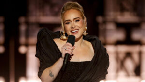 Adele performing live on stage, wearing a black gown and holding a microphone.