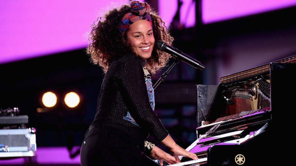 Alicia Keys performing on a grand piano during a live concert, showcasing her musical talent and stage presence.