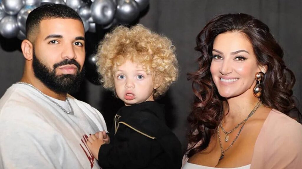 Drake standing beside Sophie Brussaux, smiling with their son Adonis between them during a public appearance.