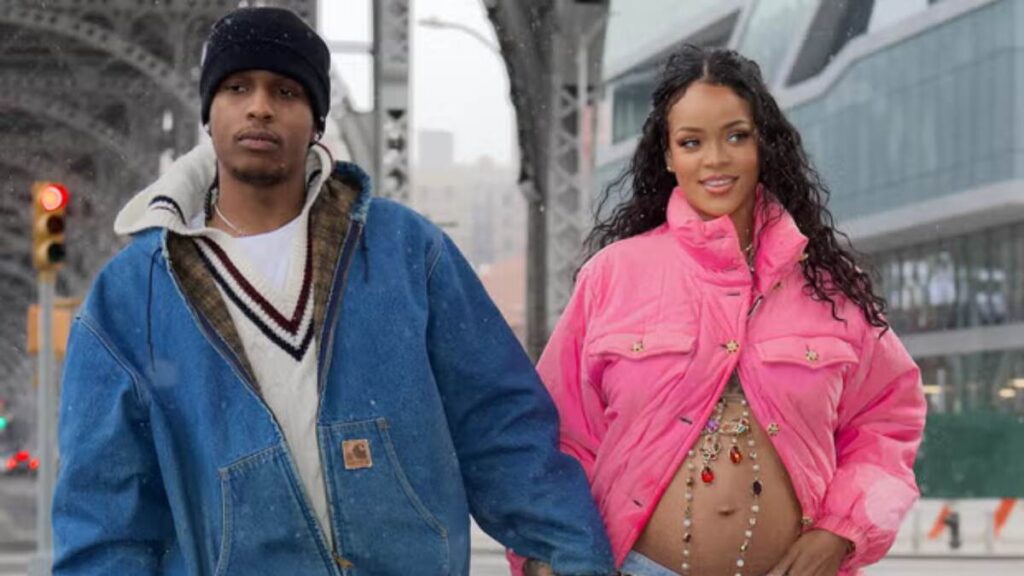 Rihanna and A$AP Rocky walking hand-in-hand on the street, with Rihanna showcasing her pregnant belly in a stylish outfit.