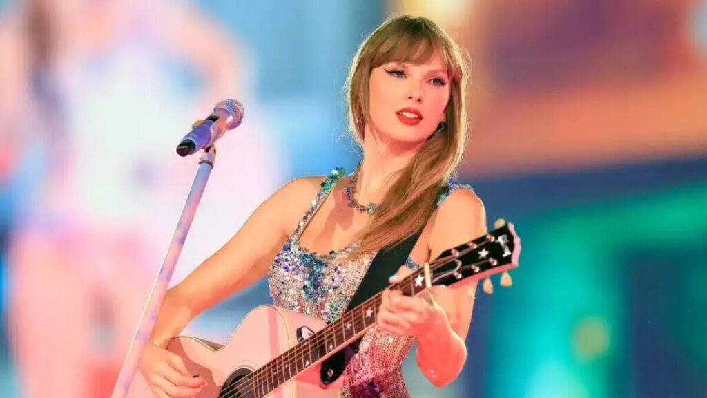 Taylor Swift performing live on stage with a guitar during a concert.