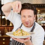 Jamie Oliver cooking on set during a TV show, preparing a meal on-camera
