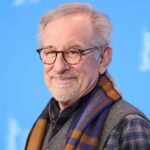 Steven Spielberg, legendary film director and producer, wearing glasses and smiling at a red carpet event.