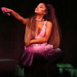 Ariana Grande performing live on stage during her 2025 concert tour, surrounded by backup dancers and LED lights.