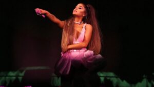 Ariana Grande performing live on stage during her 2025 concert tour, surrounded by backup dancers and LED lights.