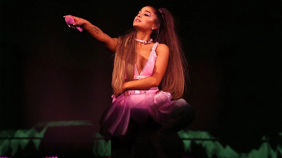 Ariana Grande performing live on stage during her 2025 concert tour, surrounded by backup dancers and LED lights.