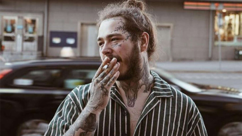 Post Malone performing live in 2019, holding a cigarette on stage, capturing his raw and unfiltered performance style.