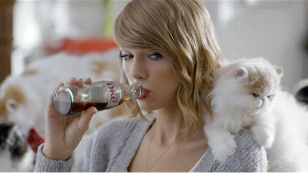 Taylor Swift in a Coca-Cola brand collaboration shoot, holding a Coke bottle with her cat Olivia Benson beside her — highlighting her personal brand integration with lifestyle marketing.